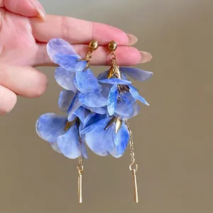 Close-up of blue raffia flower drop earrings with gold bar detailing.