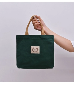Detailed close-up of dark green canvas tote bag featuring a cute cartoon bear patch