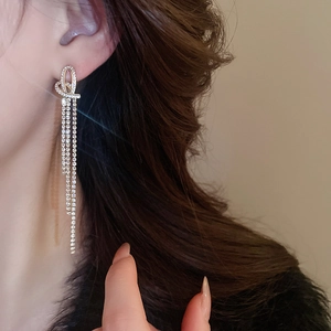 Close-up of sparkling rhinestone heart knot tassel earrings worn on a model's ear