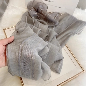 Detailed view of grey silk wool scarf with metallic stripes on white faux fur background