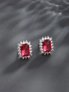 Macro shot of rectangular ruby earrings with white zircon halo on grey texture