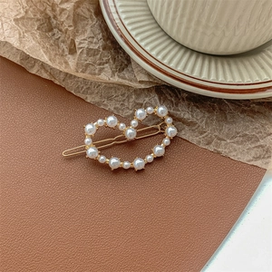 Detail of a heart-shaped gold hair clip with white pearls on a brown leather surface