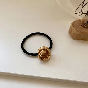 Macro detail of minimalist gold multi-loop metal knot on high-elasticity black hair tie