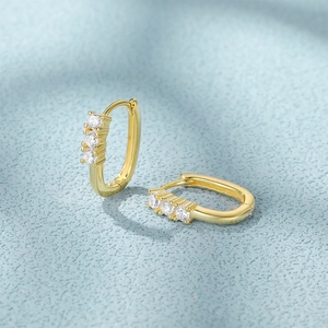 Detail shot of small gold C-shaped hoop earrings with three sparkling round zircons