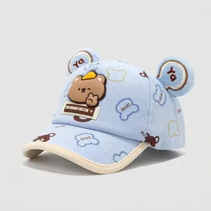 Detalle de gorra infantil azul claro con orejas de oso 3D y logotipos estampados