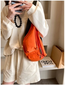 Detail of bright orange crossbody bag featuring triple zipper compartments and wide strap