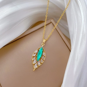 Elegant gold titanium necklace with emerald leaf pendant on white tulle background