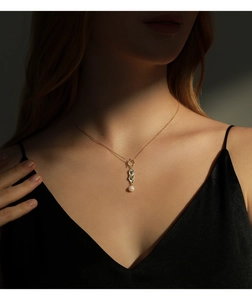 Detail view of a gold chain necklace with a textured ripple pendant and a white pearl charm