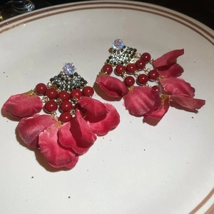 Macro detail of red fabric flower petals and tassel drop earrings with crystal studs