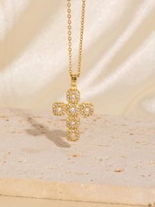 Macro shot of gold cross pendant with white zircon pavé on beige stone and silk