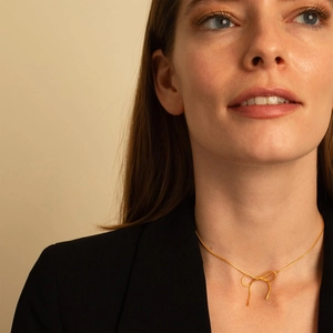 Elegant gold bow pendant necklace with slim snake chain shown on model in natural light