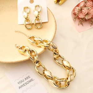 Exaggerated chunky gold chain necklace and matching earrings set on a beige ceramic plate