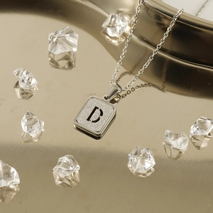 Collana in acciaio argento con ciondolo quadrato sabbiato lettera D su vassoio dorato