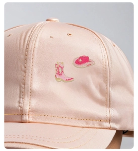 Macro shot of pink enamel cowboy boot and hat badges pinned to a satin baseball cap