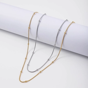 Detail of 18K gold and silver plated snake chains with small beads on a white pedestal