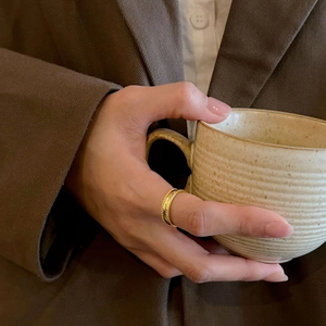 Close-up of a wide gold ring with beaded edge detail worn on a model holding a cup
