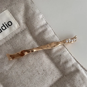 Detail of wavy gold metal hair clip with four inlaid pearls on beige linen bag