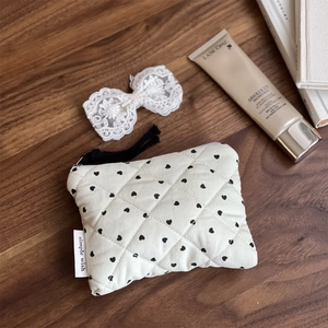 Quilted corduroy pouch with heart print and tassel detail shown with cosmetics on wood table
