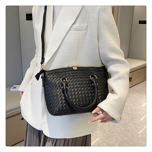 Détail du sac cabas tressé noir avec boucles dorées porté avec une tenue blanche chic