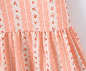 Dettaglio del tessuto floreale rosa con rose rosse e pizzo bianco sull'abito a balze
