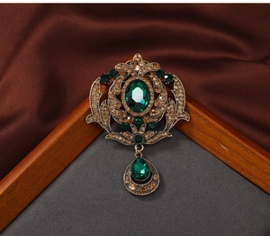 Detailed macro of vintage palace style brooch with green oval gemstone and amber rhinestones