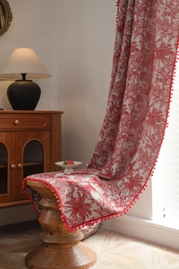 Detail of red French pattern curtain with decorative pom poms on a wooden stool