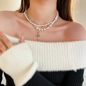 Close-up of layered necklace with silver cross pendant and pearls on model neck
