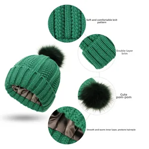 Detail view of green knit beanie featuring a faux fur pom and smooth satin hair-care lining