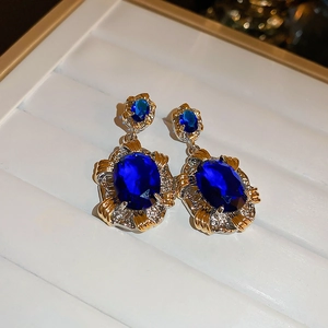 Macro detail of oval blue gemstone earrings with gold floral silver needle setting