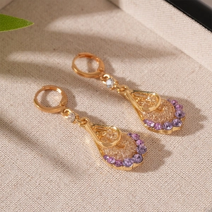 Detail of vintage gold drop earrings with mesh pattern and purple zircon stones on linen