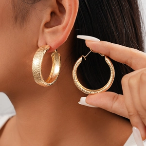 Detail of gold textured hoop earring with snakeskin pattern shown on ear and held by hand