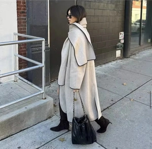 Street style view of a beige oversized wool coat with black piping detail and draped fit