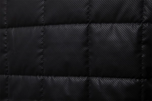 Close-up of black quilted fabric with fine diagonal carbon fiber texture and stitching