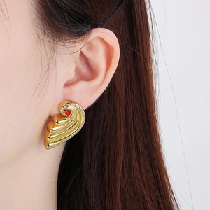 Detailed view of gold wing-shaped earrings with red gemstone and micro-pave crystals