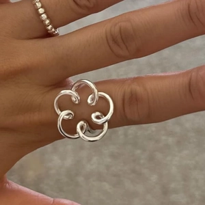 Detail of 925 sterling silver hollow flower ring with polished intersecting bands on finger