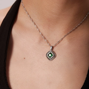 Detailed view of square green gemstone pendant on a silver necklace worn by a model