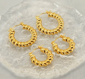 Macro shot of two pairs of golden twisted hoop earrings on a decorative glass tray