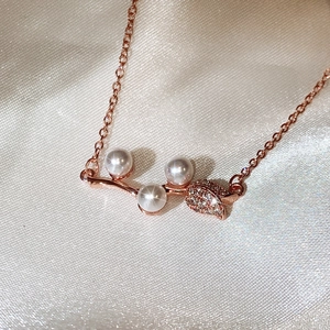 Close-up of rose gold necklace with three pearls and zircon leaf on silk background