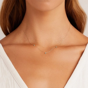 Close-up of minimalist gold thin chain necklace with turquoise blue beads on woman's neck