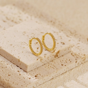 Macro shot of gold-plated hinged hoop earrings with pavé crystals on a stone surface