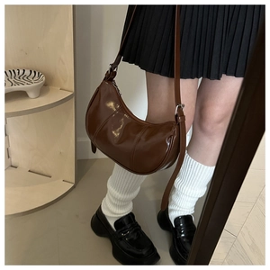Close-up of brown glossy crescent bag with adjustable strap in preppy style fashion
