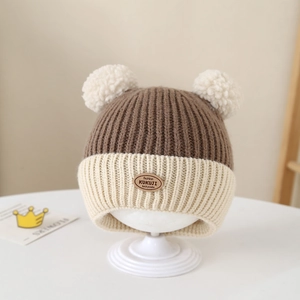 Detailed close-up of baby knit hat with brown beige stripes and two white faux fur pom-poms