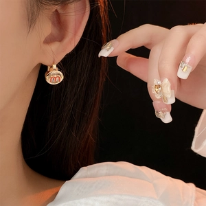 Close-up of golden letter M hoop earring with red enamel on model's ear