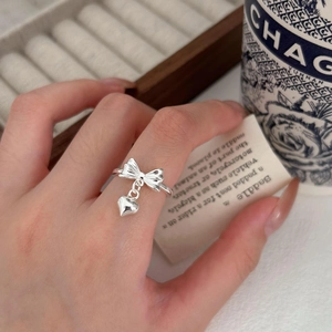 Detail of S925 sterling silver bow ring with heart pendant on hand with vintage props