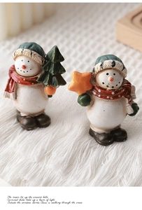 Detail of two resin snowman figurines with Christmas hats on soft white plush background