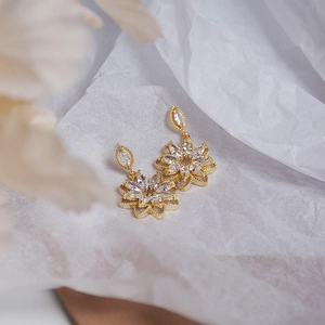 Macro shot of gold floral earrings with clear zircon crystals on white crinkled paper