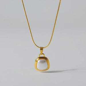 Detail of a square gold pendant necklace with a white pearl inlay on a snake chain