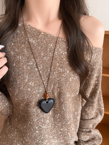 Gros plan d'un pendentif cœur noir mat avec perle ambrée sur cordon brun sur un tricot