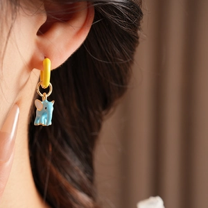 Close-up of cute blue elephant enamel earrings with yellow hoop on model's ear