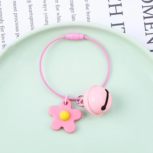 Close-up of a pink floral keychain with a round bell and wire ring on a green dish